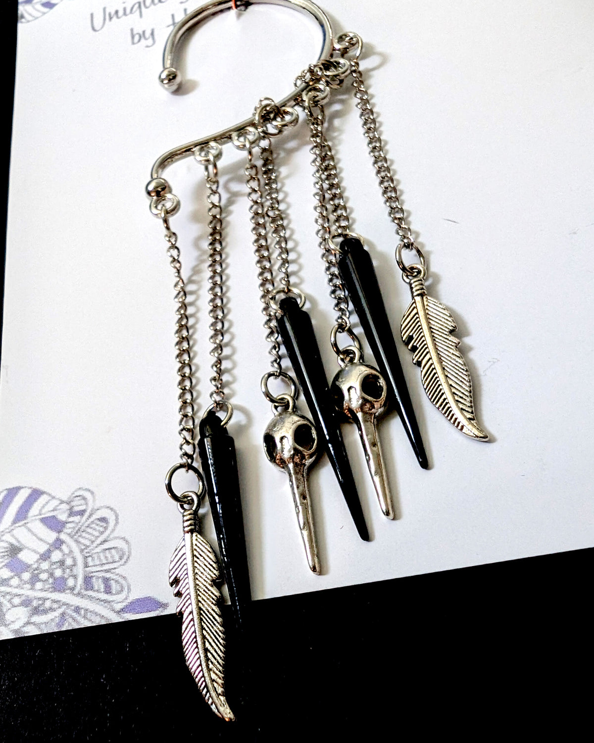 Close-up view of the silver bird skull ear cuff showcasing the hanging chains, black spikes, metal bird skull charms, and detailed feather pendants.