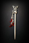 Isolated product shot of the silver hair pick against a black background, featuring a tapered shaft, a skull topper with a perched winged cat creature, and three dangling chains with silver stars and red glitter resin crescent moons.