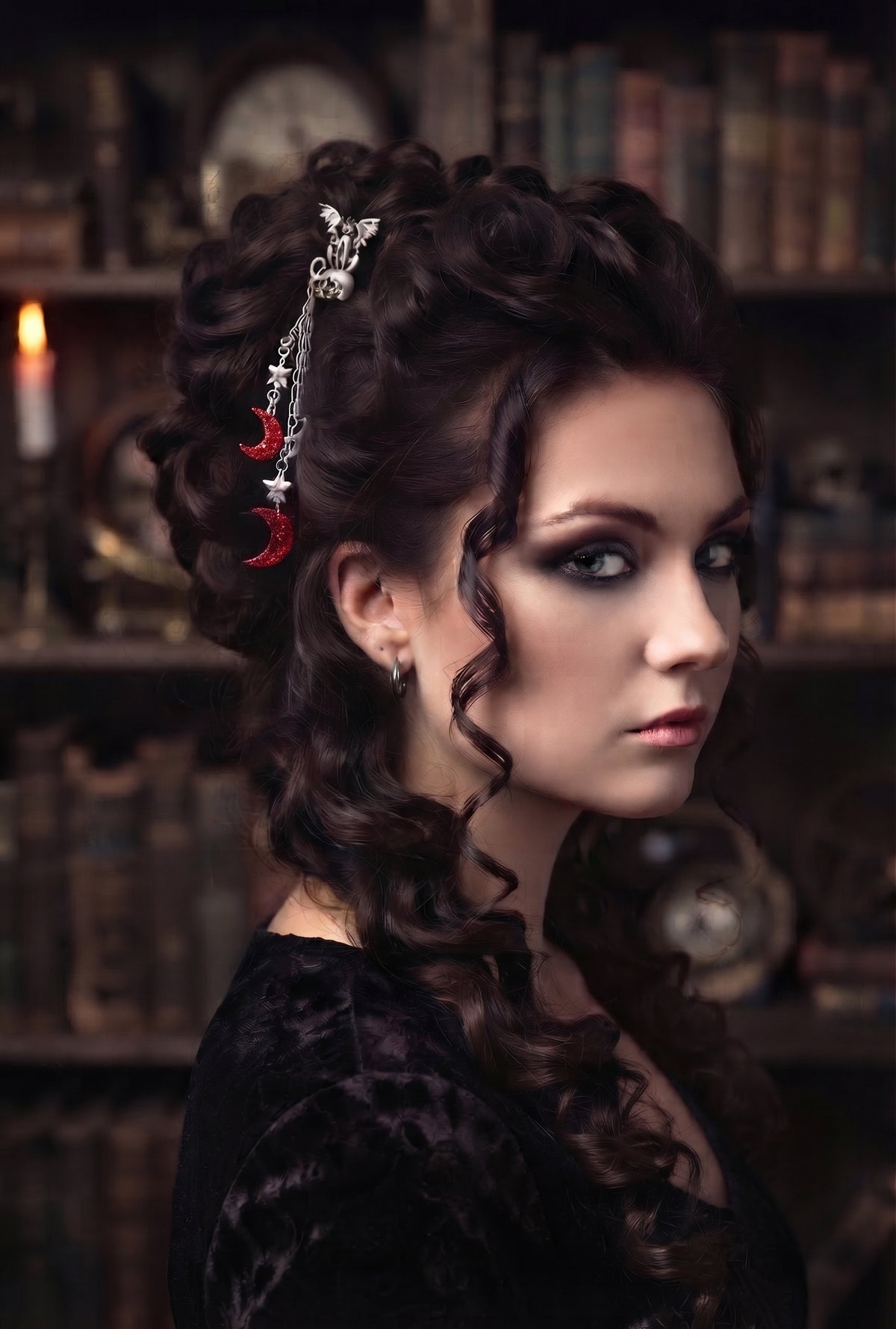 Side profile of a model with dark, curly updo hair styled with the silver winged cat and skull hair pick, set against a dark bookshelf backdrop.