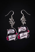 Wanna Give You The Creeps Earrings by Circle of Heather, full view of both printed acrylic charms reading "I just wanna give you the creeps" with silver-tone leaf branches and fishhook earwires, on a plain black background.