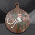 Dystopian Cyclopean by CamiThunderInk, an original pyrography and paint piece on a reclaimed round wood paddle showing a one eyed skull with tusks among pink chrysanthemums and green cedar