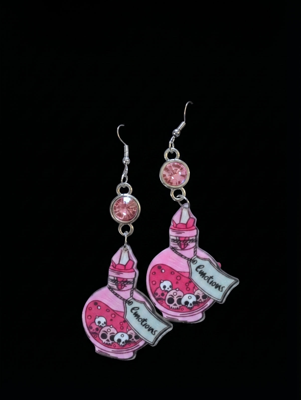 A pair of dangling earrings featuring pink illustrated potion bottles with cartoon faces and the text 'Immortal Elixir' on a black background.