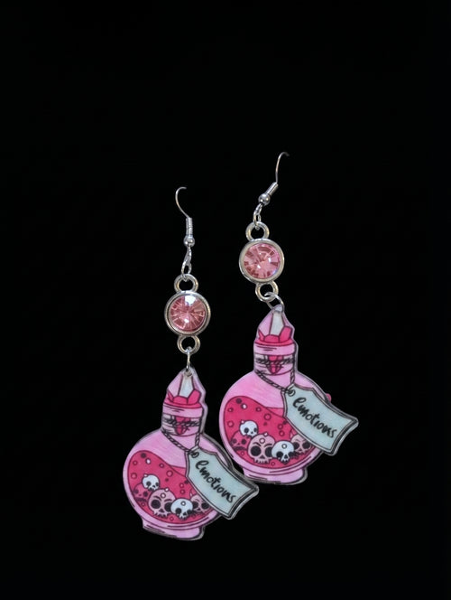 A pair of dangling earrings featuring pink illustrated potion bottles with cartoon faces and the text 'Immortal Elixir' on a black background.