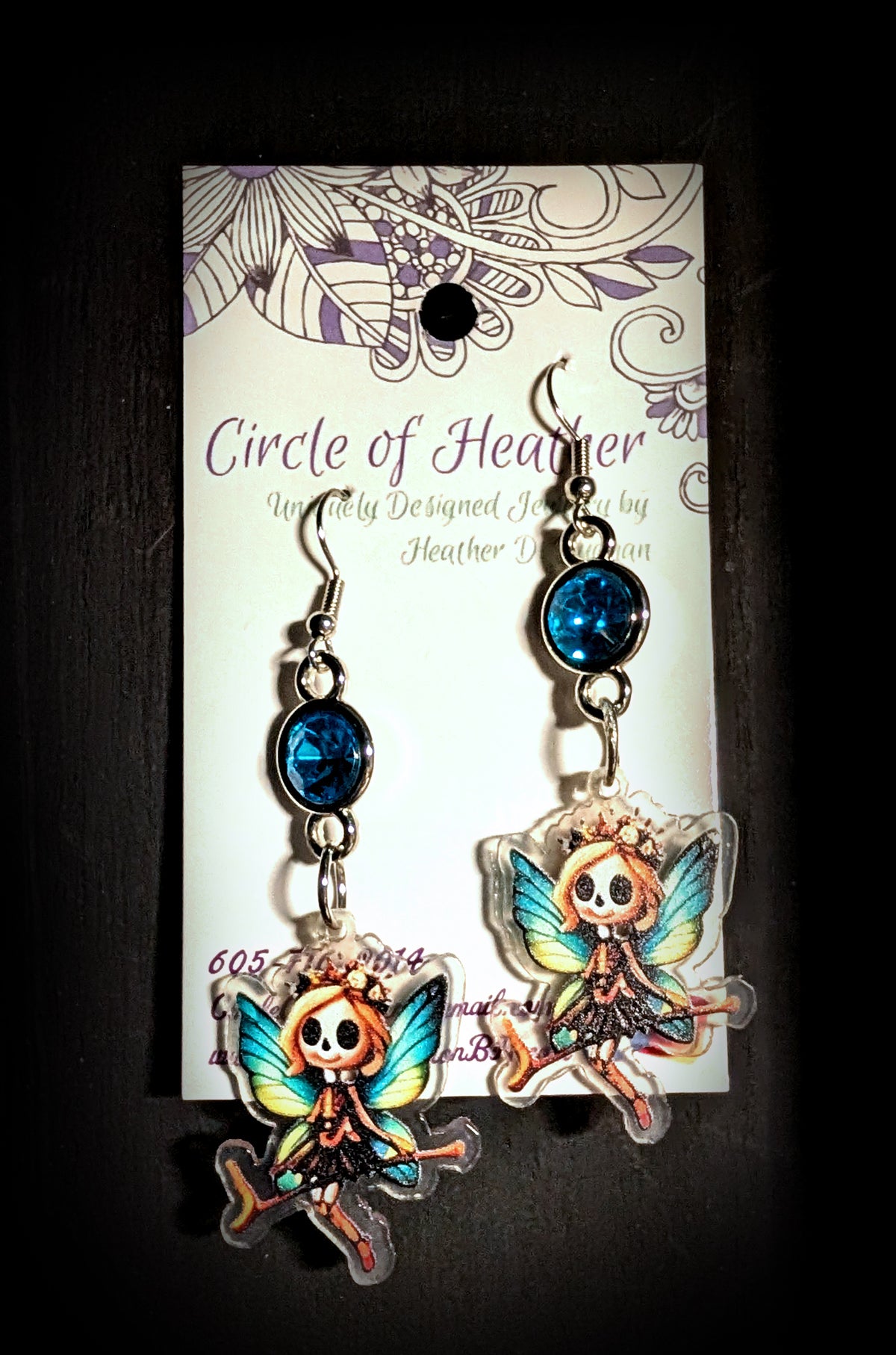 Flower Crown Skull Fairy Earrings by Circle of Heather, blue rhinestone tops and printed acrylic fairy charms with orange hair and dark tutus, shown on the branded Circle of Heather card.
