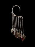 Isolated product shot of the complex silver ear cuff against a pure black background, featuring a multi-chain fringe with dangling bronze, red, and gold diamond charms and silver rods.