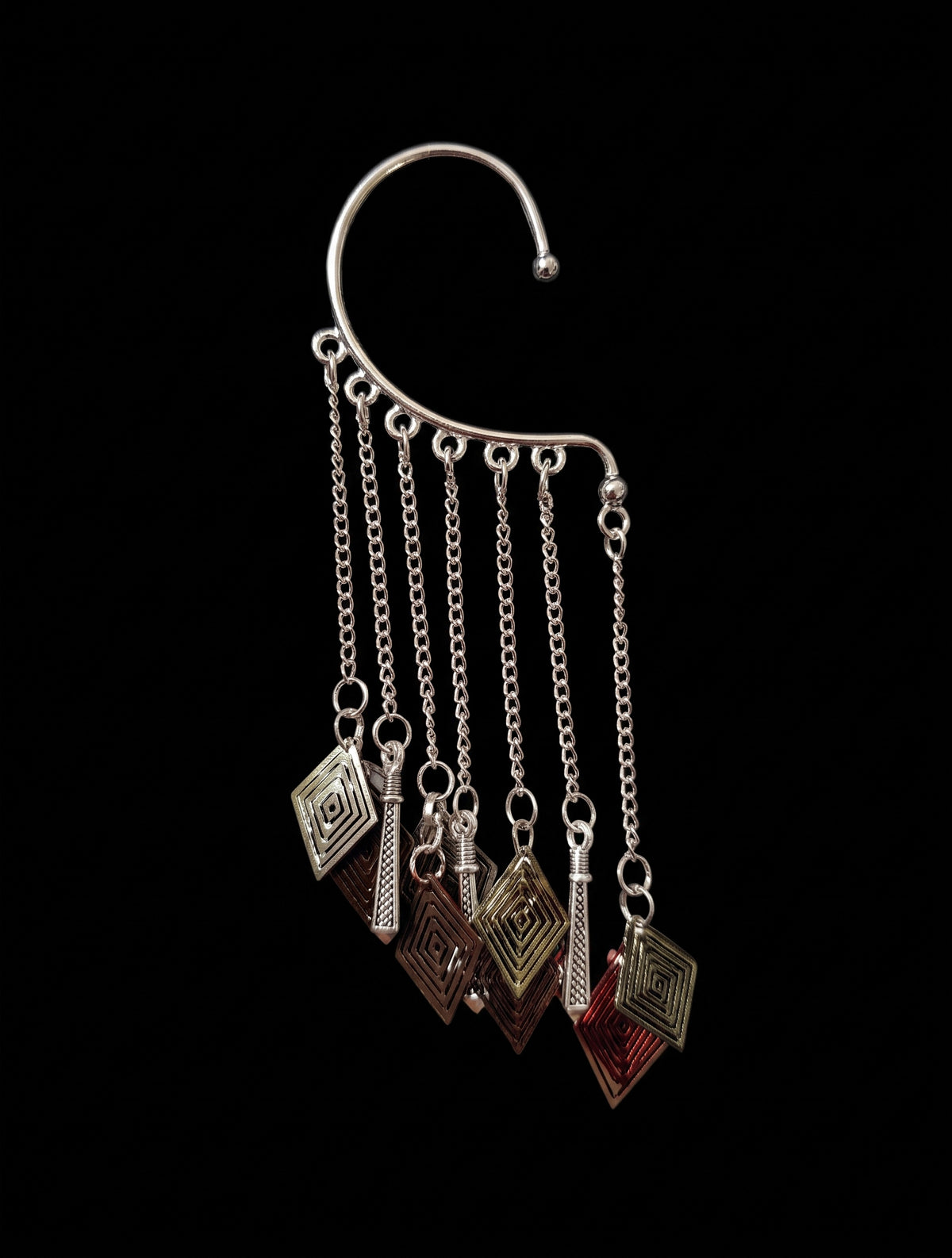 Isolated product shot of the complex silver ear cuff against a pure black background, featuring a multi-chain fringe with dangling bronze, red, and gold diamond charms and silver rods.