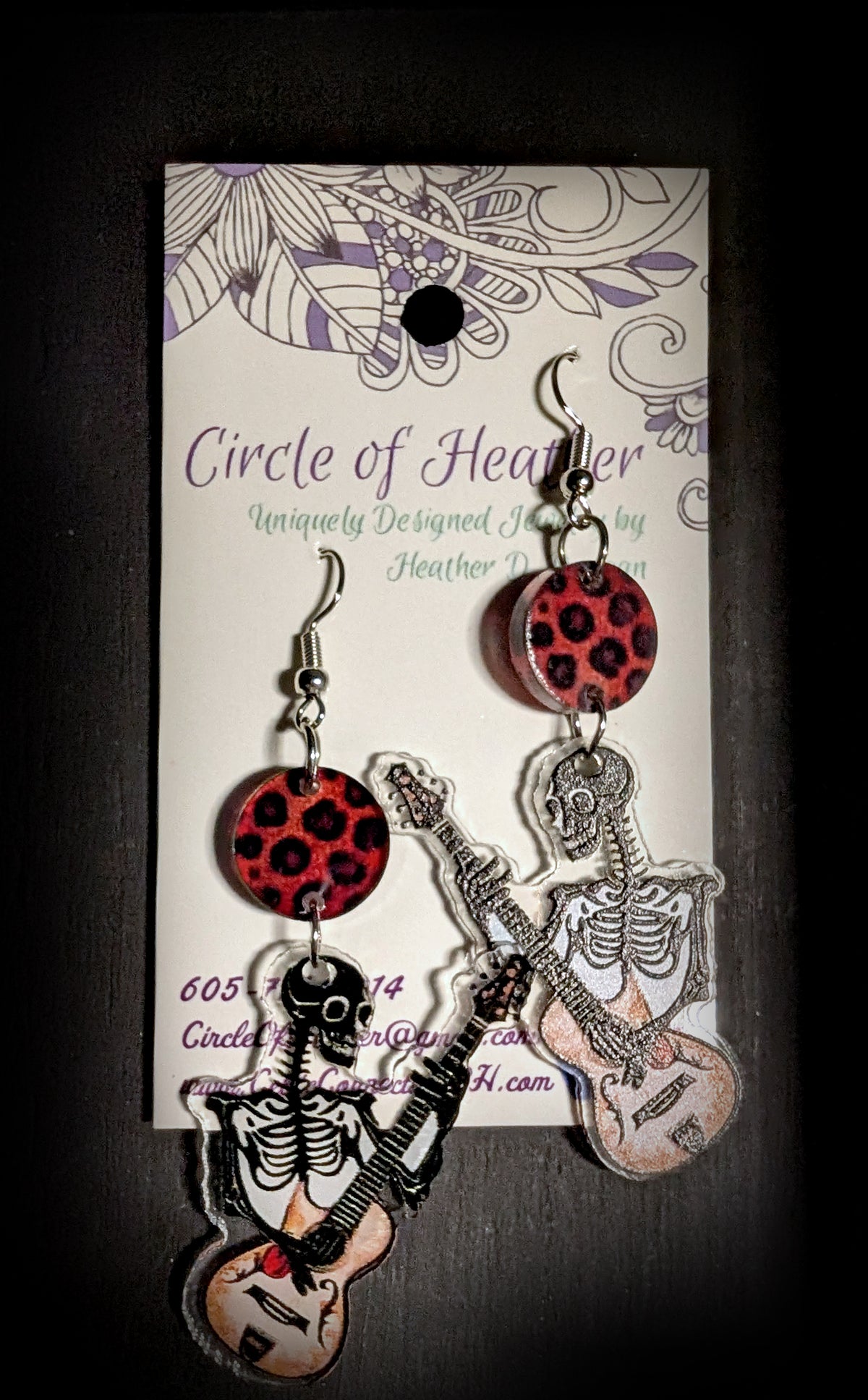Guitar Ghoul Earrings by Circle of Heather, both earrings shown on the branded Circle of Heather card with leopard print discs and skeleton guitar charms.