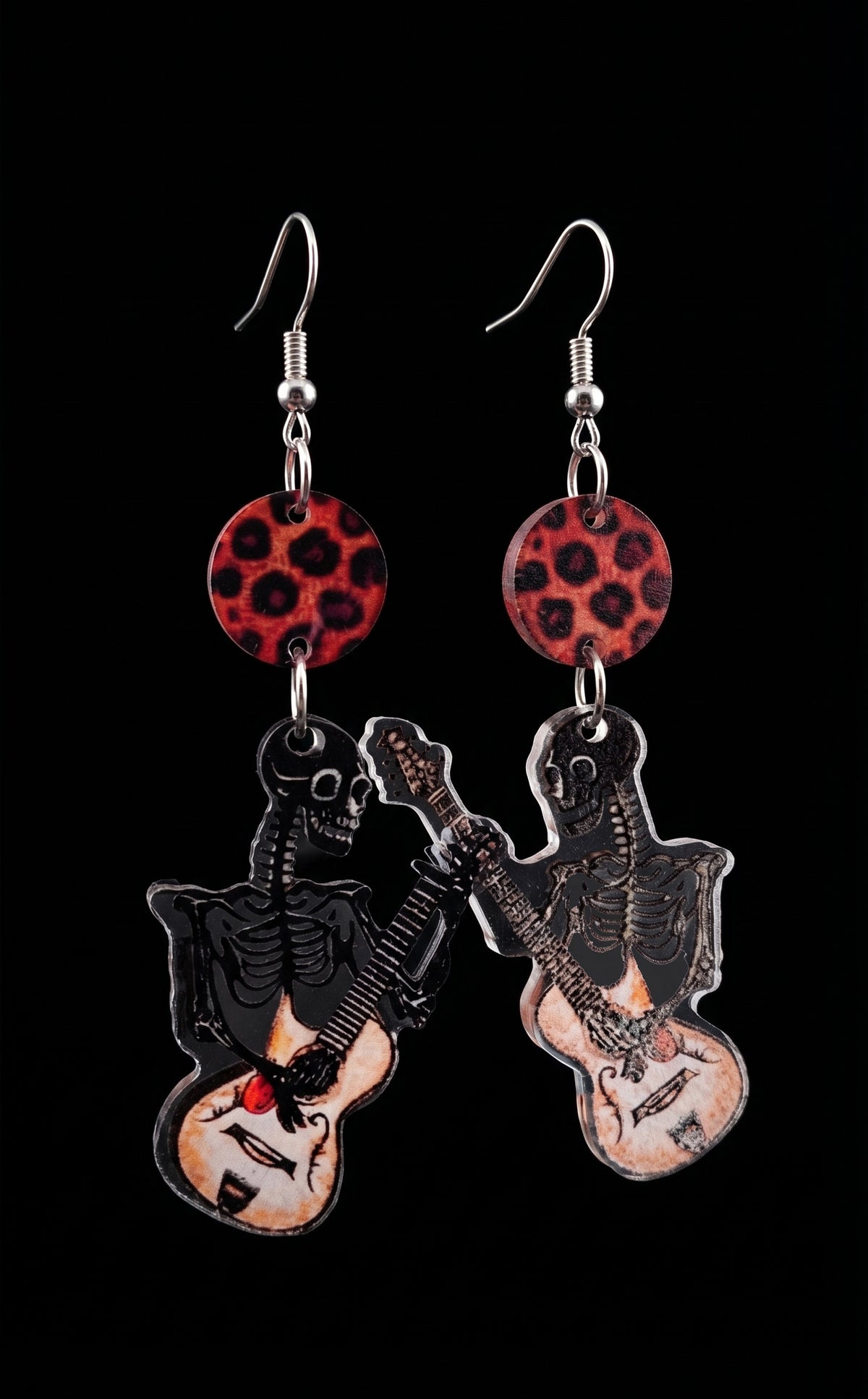 Guitar Ghoul Earrings by Circle of Heather, full view of both mirrored charms showing the skeleton linework and cream hollow-body guitars with leopard print disc tops, on a plain black background.