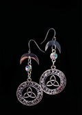 Knotted Luna Trinity Earrings by Circle of Heather, full view of both earrings showing the crescent moon, iridescent faceted stone and trinity knot inside the knotwork medallion, on a plain black background.