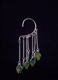 Full product shot of the silver leaf ear cuff displayed against a plain dark background, highlighting the vertical chain fringe and leafy charms.