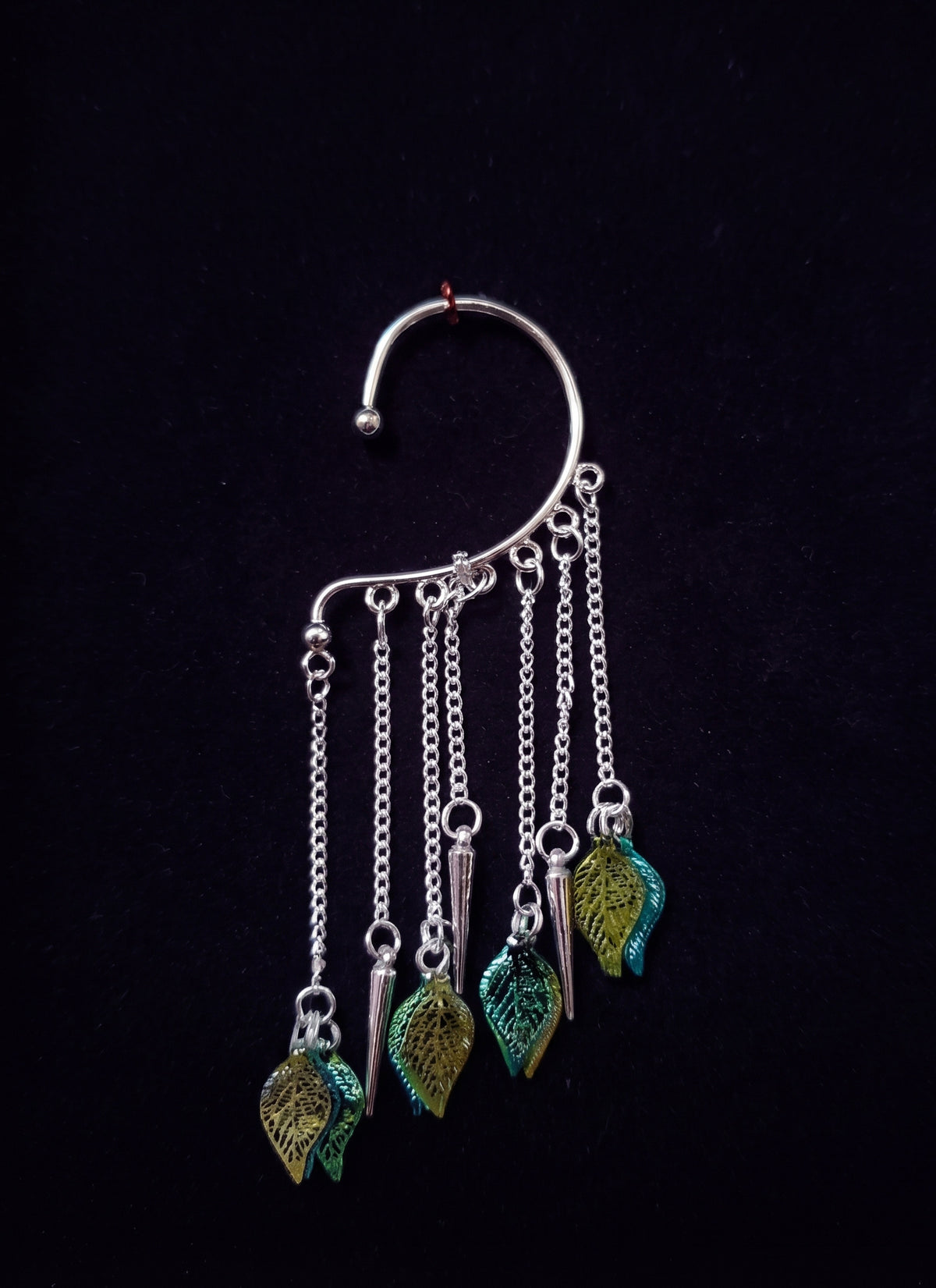 Full product shot of the silver leaf ear cuff displayed against a plain dark background, highlighting the vertical chain fringe and leafy charms.