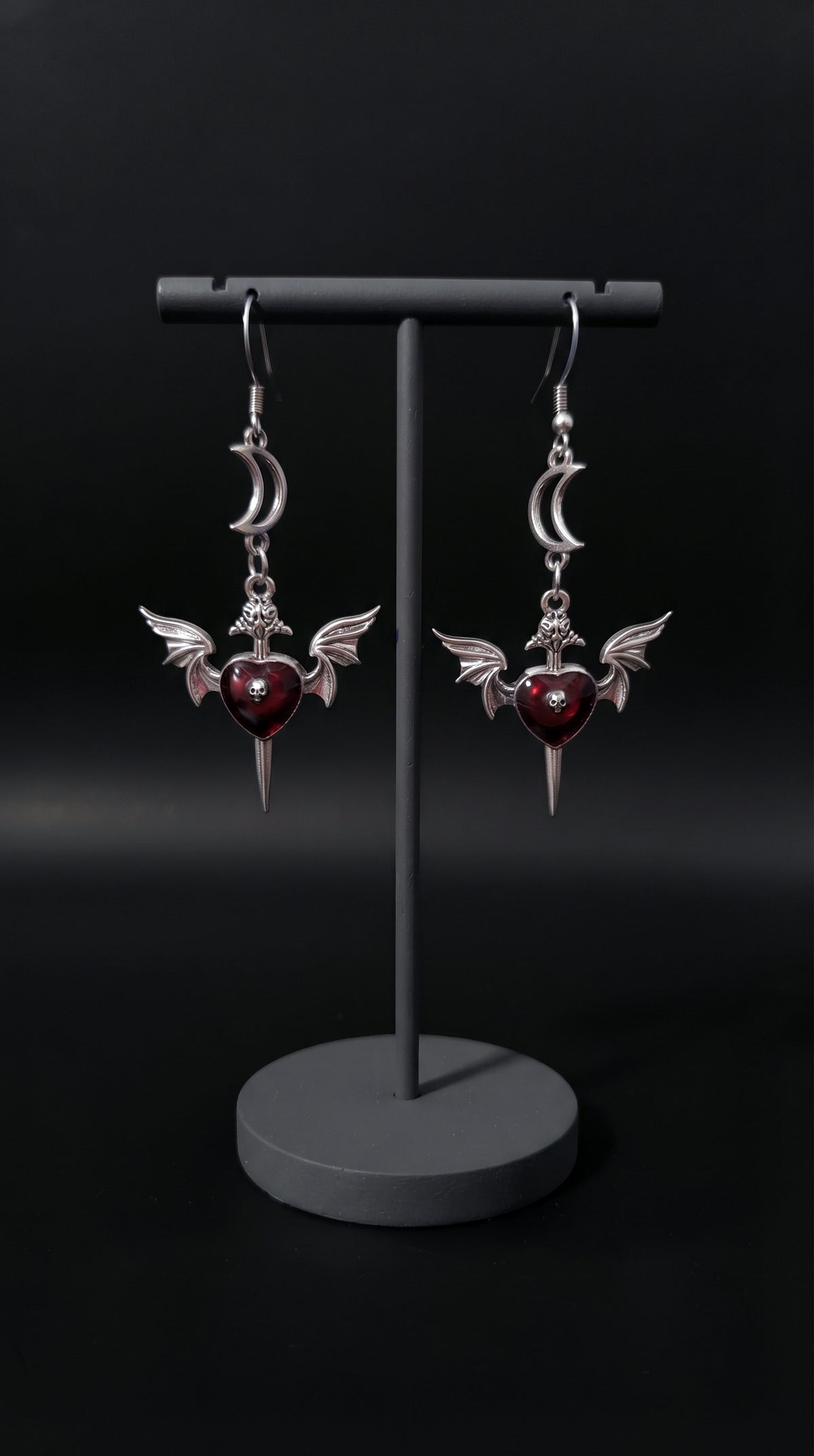 Love Soars Earrings by Circle of Heather displayed on a black earring stand, showing the crescent moon, winged heart, and dagger charm design