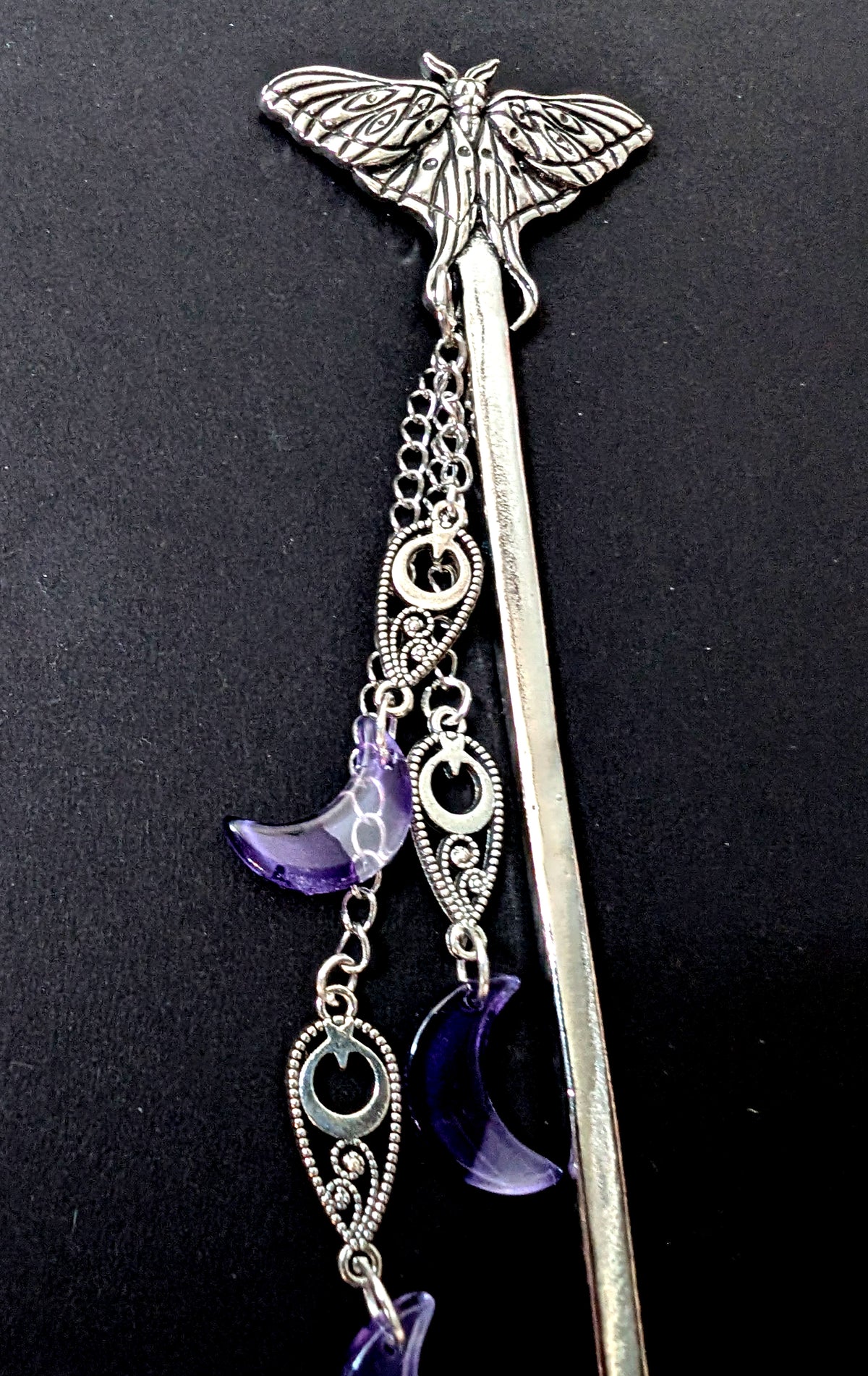 A close-up detail shot focusing on the intricate silver moth topper and the upper sections of the dangling chains, filigree work, and deep purple resin crescent moon pendants.