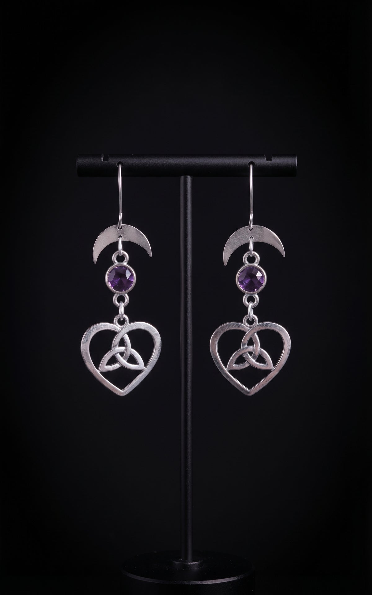 Lunar Love Trinity Earrings by Circle of Heather, full view of both earrings showing the crescent moon, faceted purple stone and open heart with trinity knot, on a plain black background.