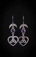 Lunar Love Trinity Earrings by Circle of Heather, full view of both earrings showing the crescent moon, faceted purple stone and open heart with trinity knot, on a plain black background.