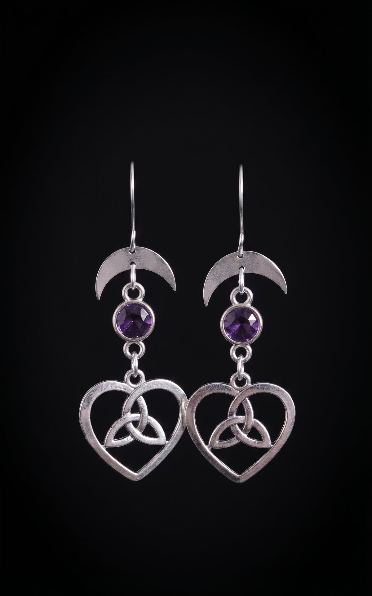 Lunar Love Trinity Earrings by Circle of Heather, full view of both earrings showing the crescent moon, faceted purple stone and open heart with trinity knot, on a plain black background.