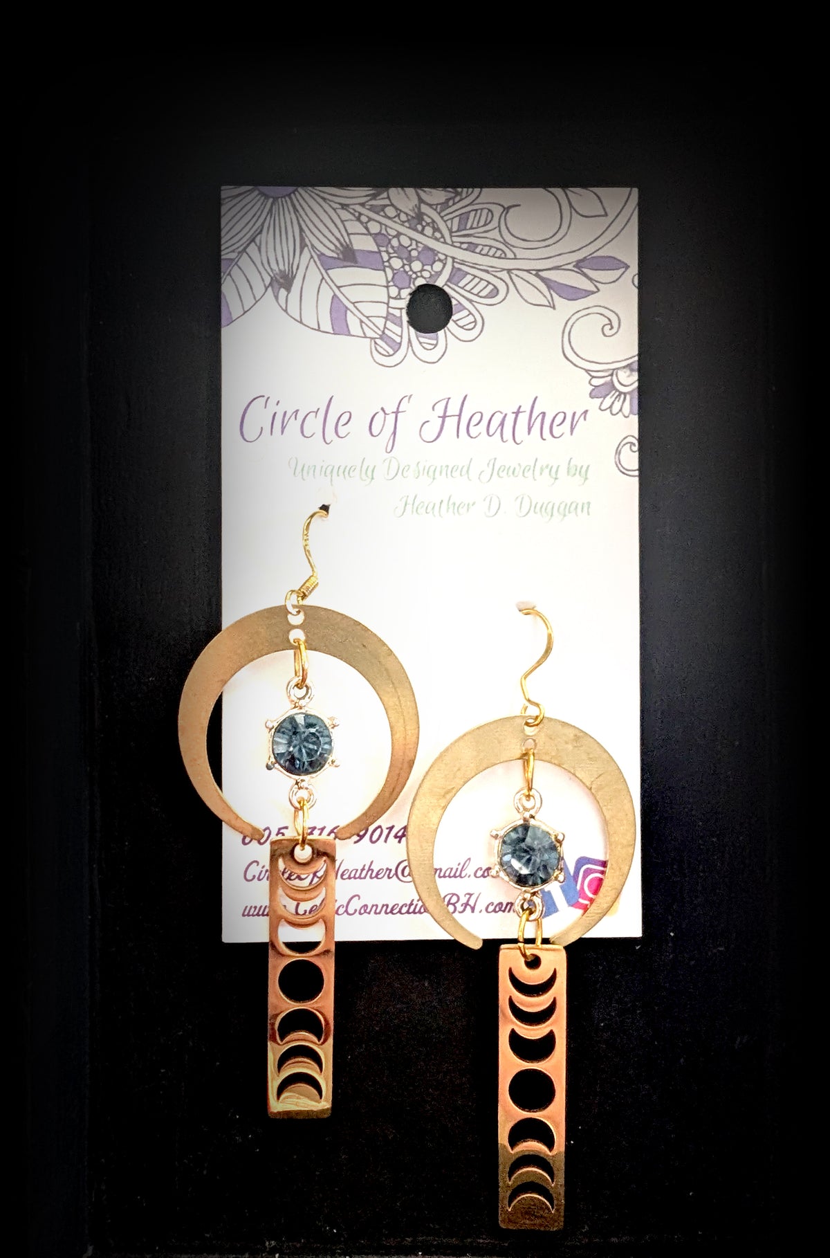 Lunar Obelisk Earrings by Circle of Heather, both earrings shown on the branded Circle of Heather card with gold crescent rings, grey blue stones and moon phase bars.