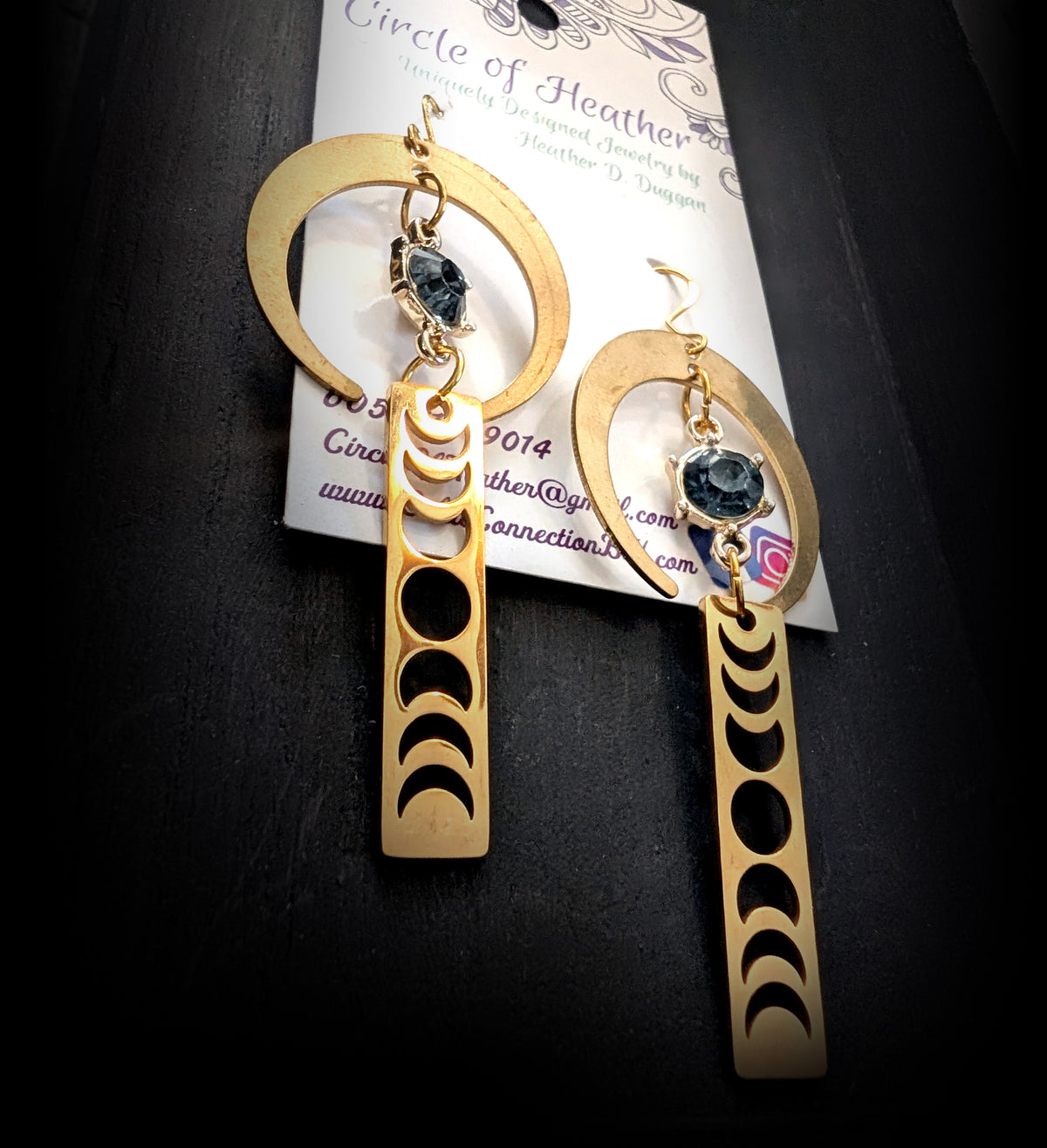 Lunar Obelisk Earrings by Circle of Heather, angled close-up showing the prong setting on the grey blue stone and the cut moon phases along the bar, shown on the branded Circle of Heather card.