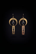 Lunar Obelisk Earrings by Circle of Heather, full view of both earrings showing the open crescent ring, prong-set grey blue stone and the moon cycle cut through the gold bar, on a plain black background.