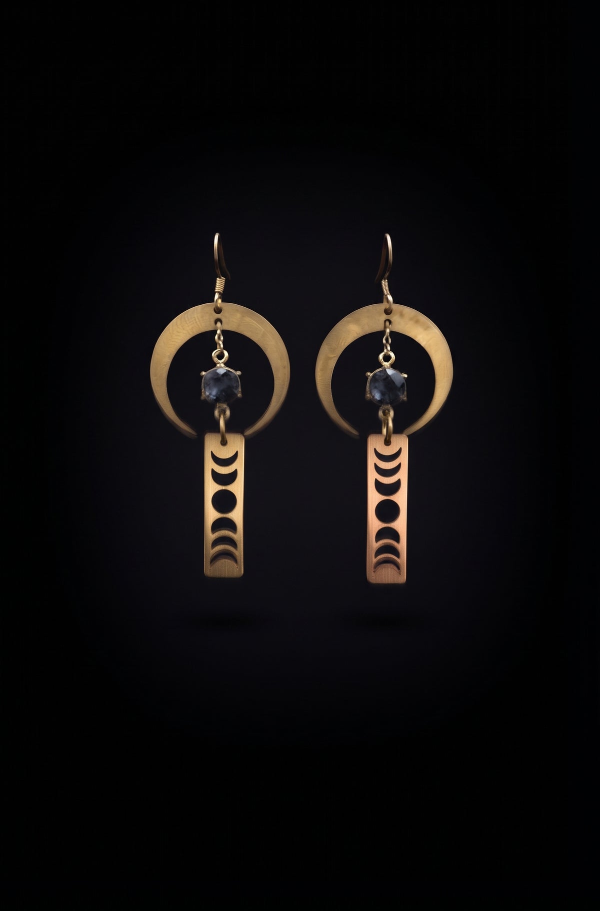 Lunar Obelisk Earrings by Circle of Heather, full view of both earrings showing the open crescent ring, prong-set grey blue stone and the moon cycle cut through the gold bar, on a plain black background.