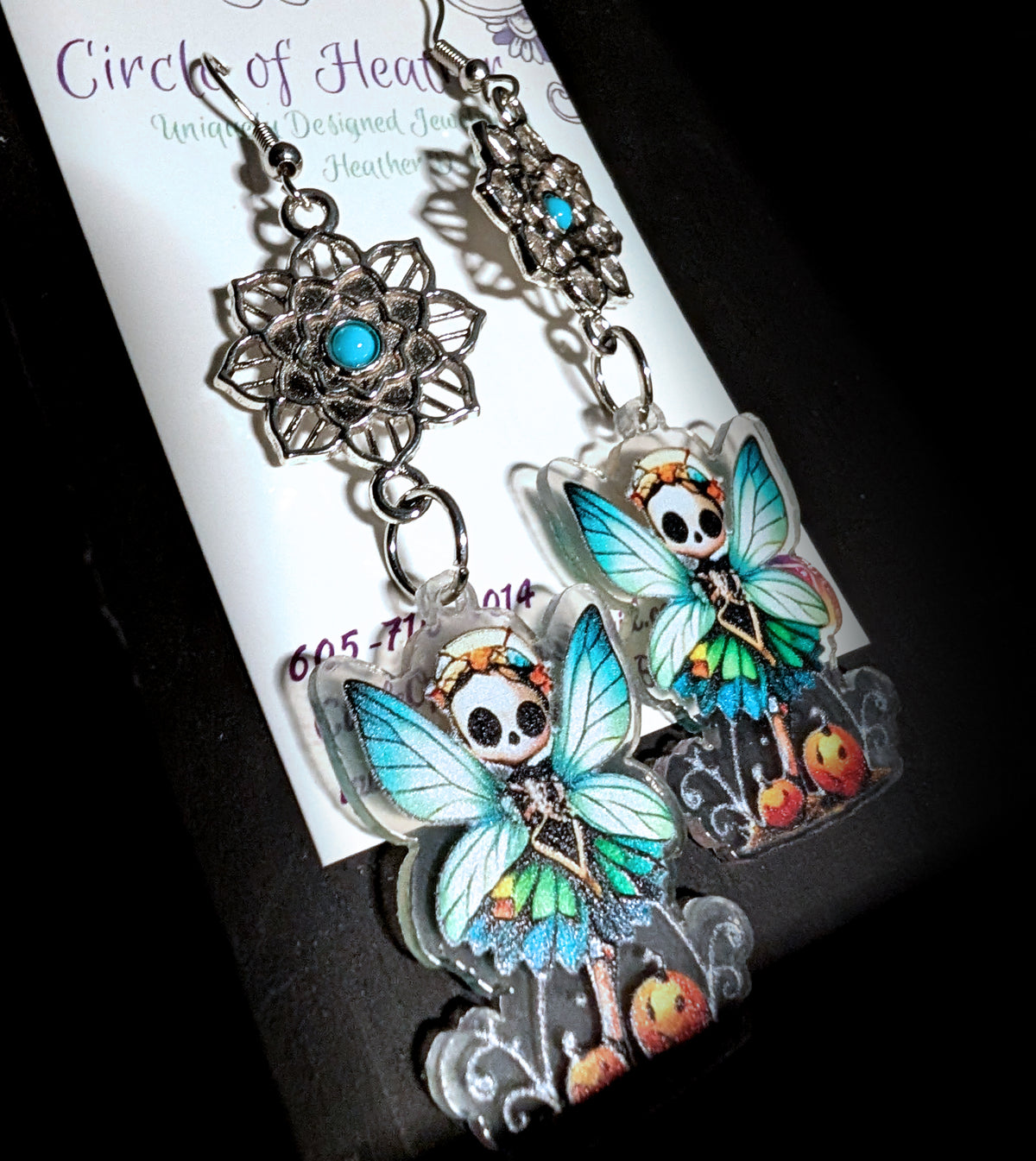 Mandala Pumpkin Skull Fairy Earrings by Circle of Heather, angled close-up showing the openwork mandala detail, turquoise cabochon and the fairy's wings and pumpkin patch artwork, shown on the branded Circle of Heather card.