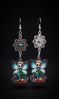 Mandala Pumpkin Skull Fairy Earrings by Circle of Heather, full view of both earrings showing the openwork mandala flowers and skull fairy charms with teal and green wings standing among orange pumpkins, on a plain black background.