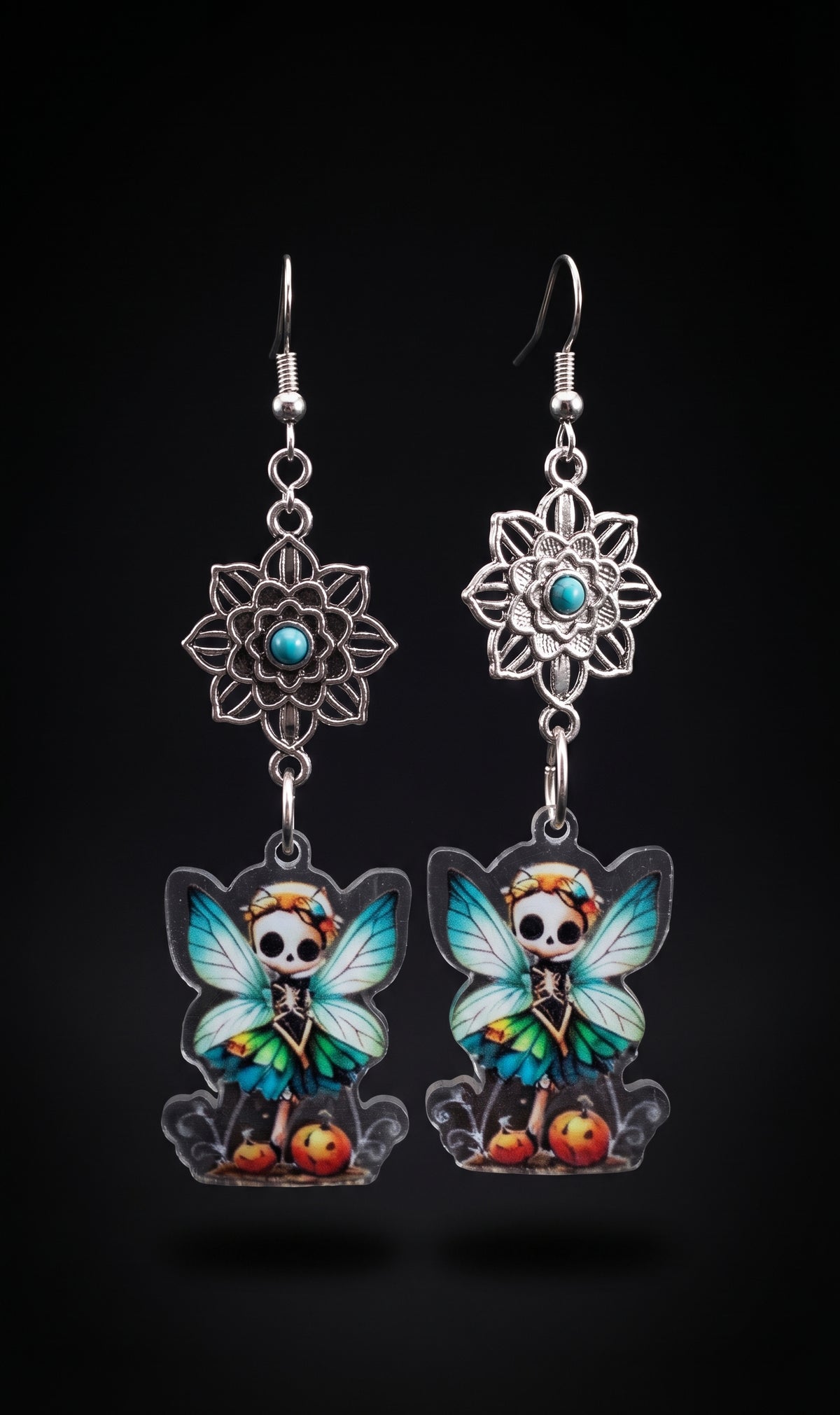 Mandala Pumpkin Skull Fairy Earrings by Circle of Heather, full view of both earrings showing the openwork mandala flowers and skull fairy charms with teal and green wings standing among orange pumpkins, on a plain black background.