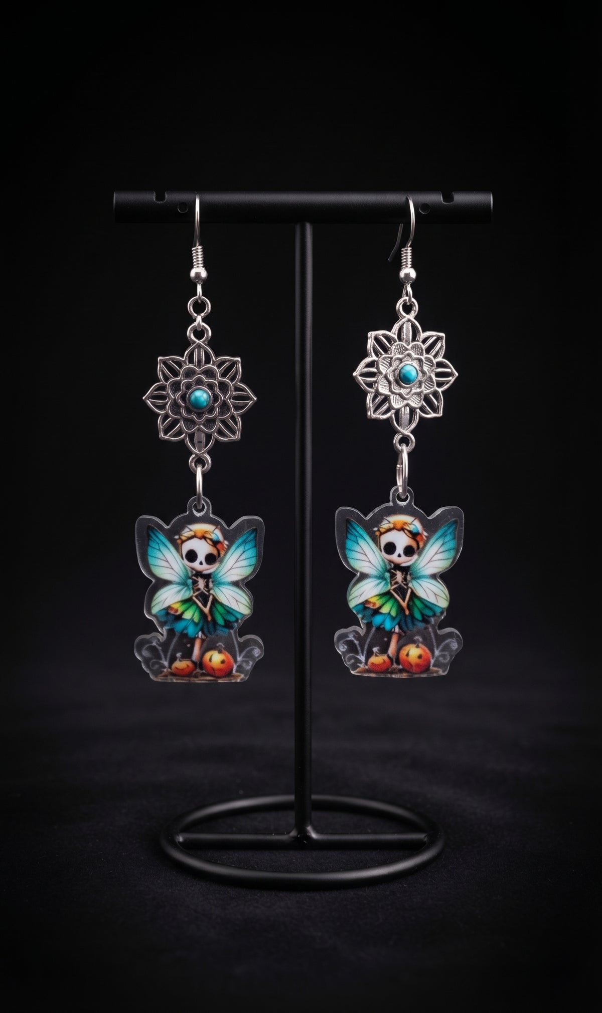 Mandala Pumpkin Skull Fairy Earrings by Circle of Heather, silver-tone mandala flowers with turquoise centers above printed acrylic skull fairy charms with pumpkins, hanging on a black T-bar jewelry stand.