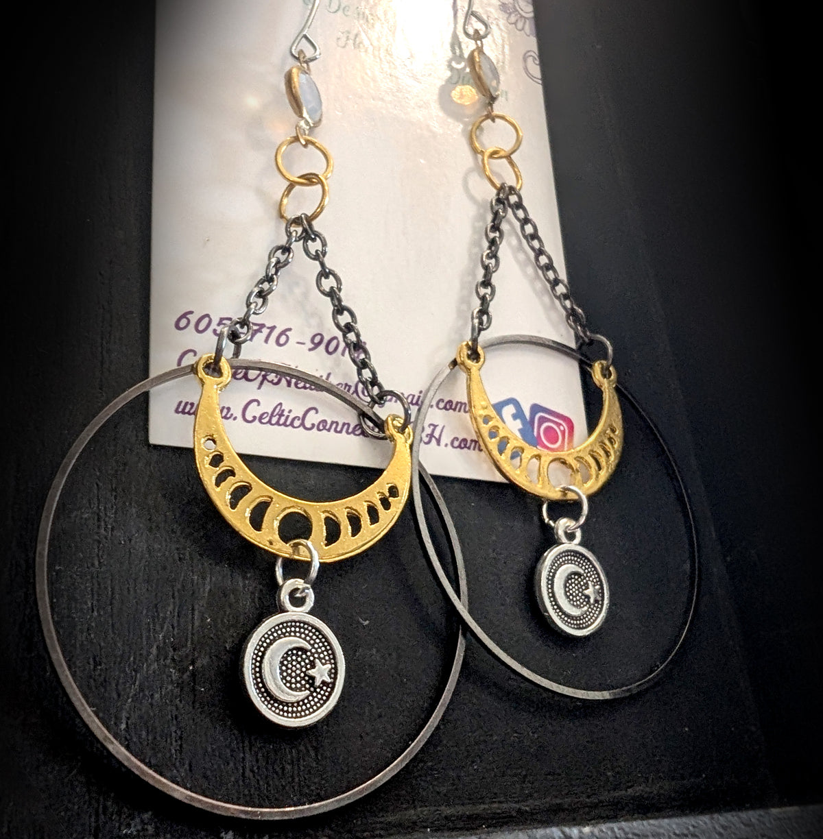Chandelier Moonphase Earrings by Circle of Heather, angled close-up of the gold moon phase crescent inside the oxidized hoop with a silver moon and star medallion hanging below, shown on the branded Circle of Heather card.