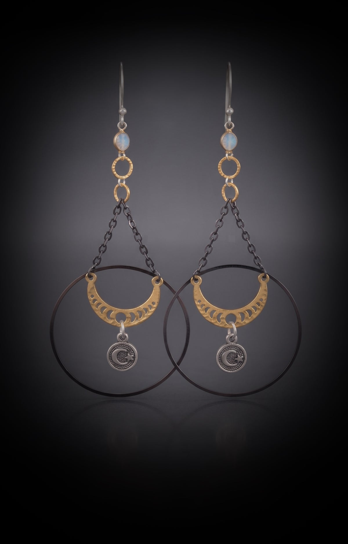 Chandelier Moonphase Earrings by Circle of Heather, full view of both earrings showing the opalescent stone top, gold rings, oxidized hoop, gold moon phase crescent and silver moon and star medallion, on a dark gradient background.