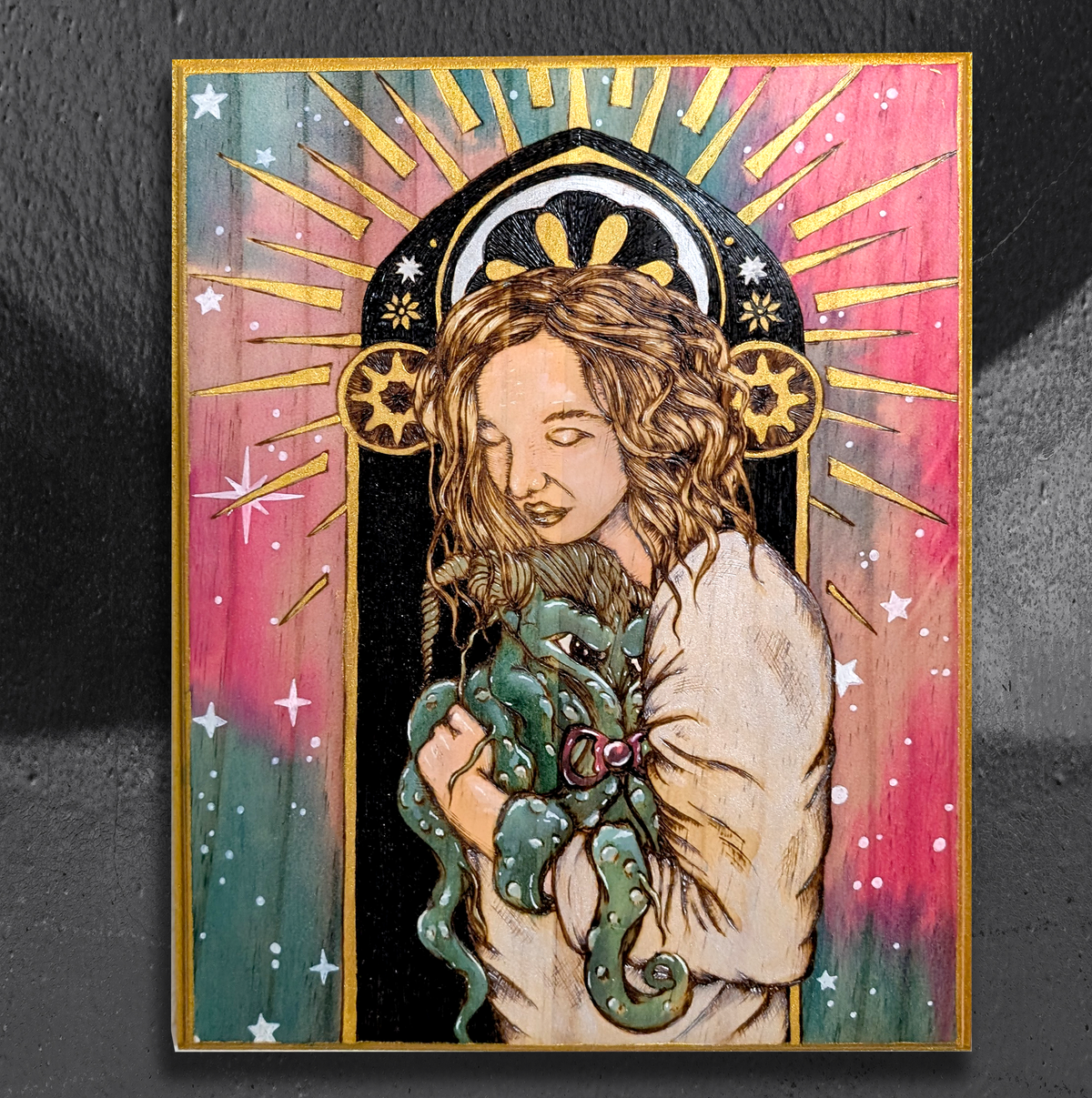 Another view of Mother of Unspeakable Evil by CamiThunderInk, an original pyrography painting on a solid wood slab of a mother cradling a baby Cthulhu with a pacifier, with a cosmic watercolor background and gold halo