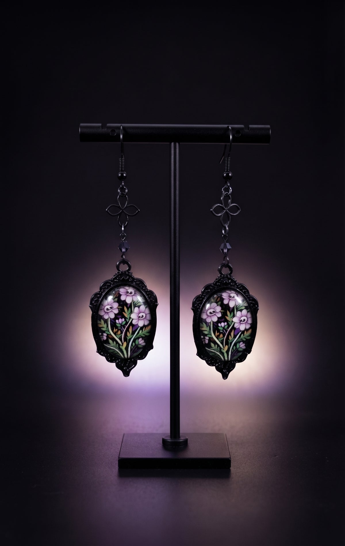 Ornamental Framed Skully Flower Earrings by Circle of Heather on a black earring stand, black filigree frames with hand-illustrated lavender skull flower artwork
