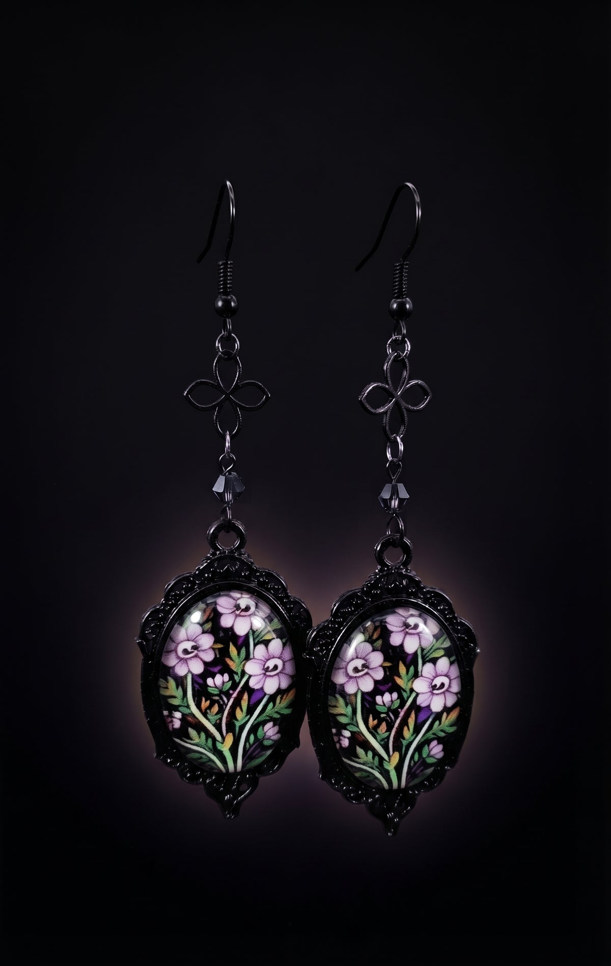 Ornamental Framed Skully Flower Earrings by Circle of Heather, black filigree oval frames with pale purple skull-faced flowers under glass, hanging from black chain with a quatrefoil link and dark crystal bead