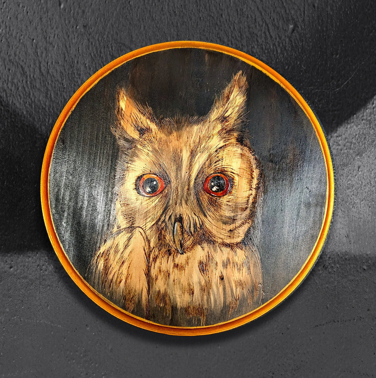 Head of Parliament by CamiThunderInk, an original pyrography and stain painting on a 12 inch pine round of a detailed long eared owl with resin eyes against a dark smoky background
