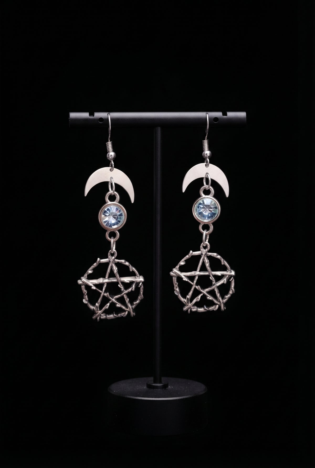 Pentacle Lunar Blue Blush Earrings by Circle of Heather, silver crescent moons with pale blue faceted stones above cast twig pentacles, hanging on a black T-bar jewelry stand.