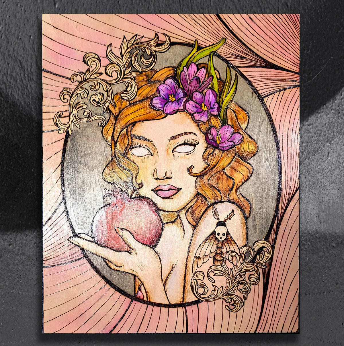 Persephone's Return by CamiThunderInk, an original Art Nouveau style pyrography and watercolor portrait of Persephone holding a pomegranate, with crocus flowers in her hair, a death's head moth tattoo, gold scrollwork, and a pink background