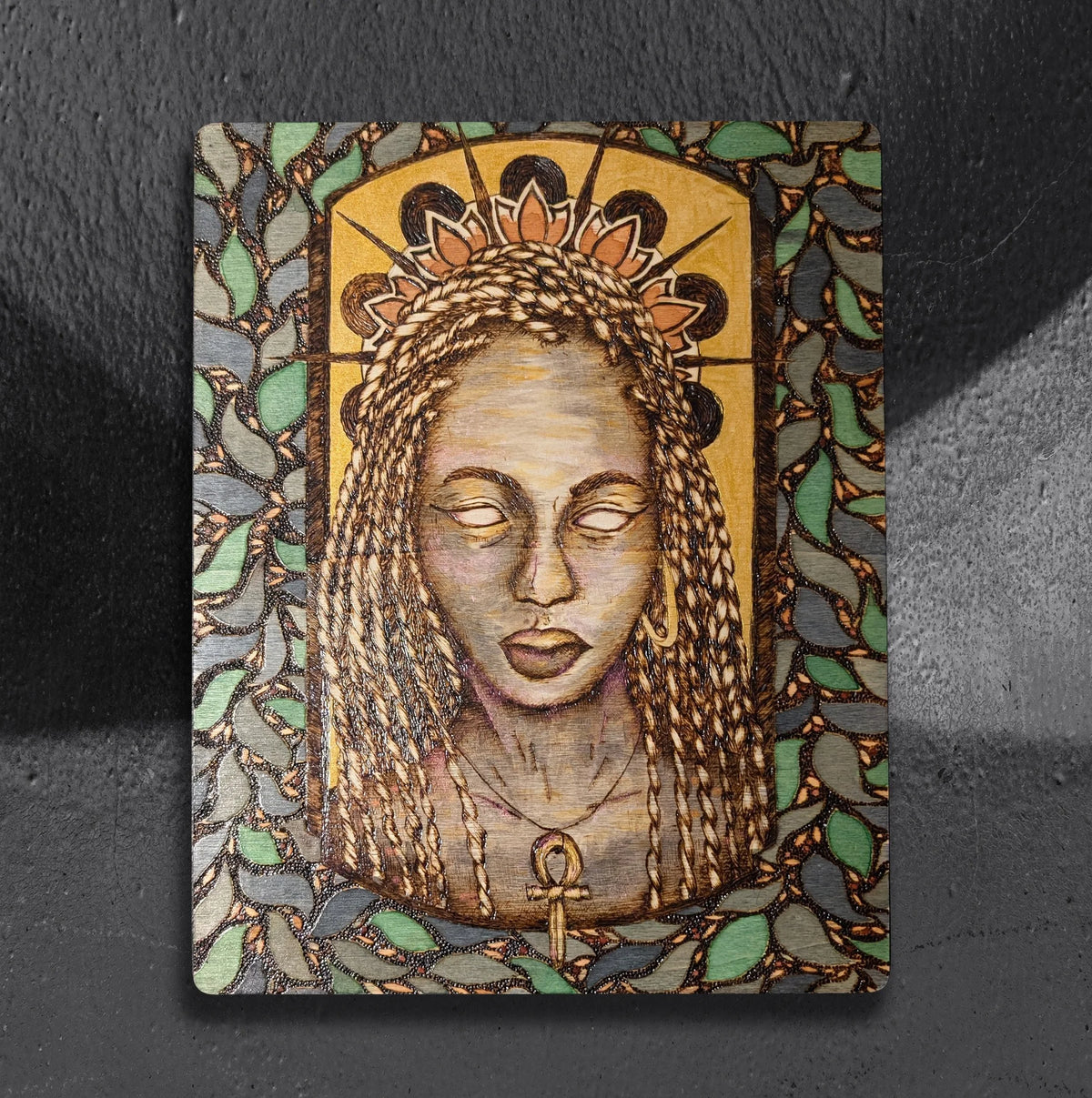 Priestess by CamiThunderInk, an original pyrography, watercolor, and gold acrylic portrait of a Black woman with long box braids, a lotus crown, and a gold ankh pendant, framed by a mosaic leaf border and a gold arch