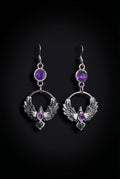 Purple Phoenix Halo Earrings by Circle of Heather, full view of both earrings showing the faceted purple stones, open circles and outstretched feathered wings, on a plain black background.