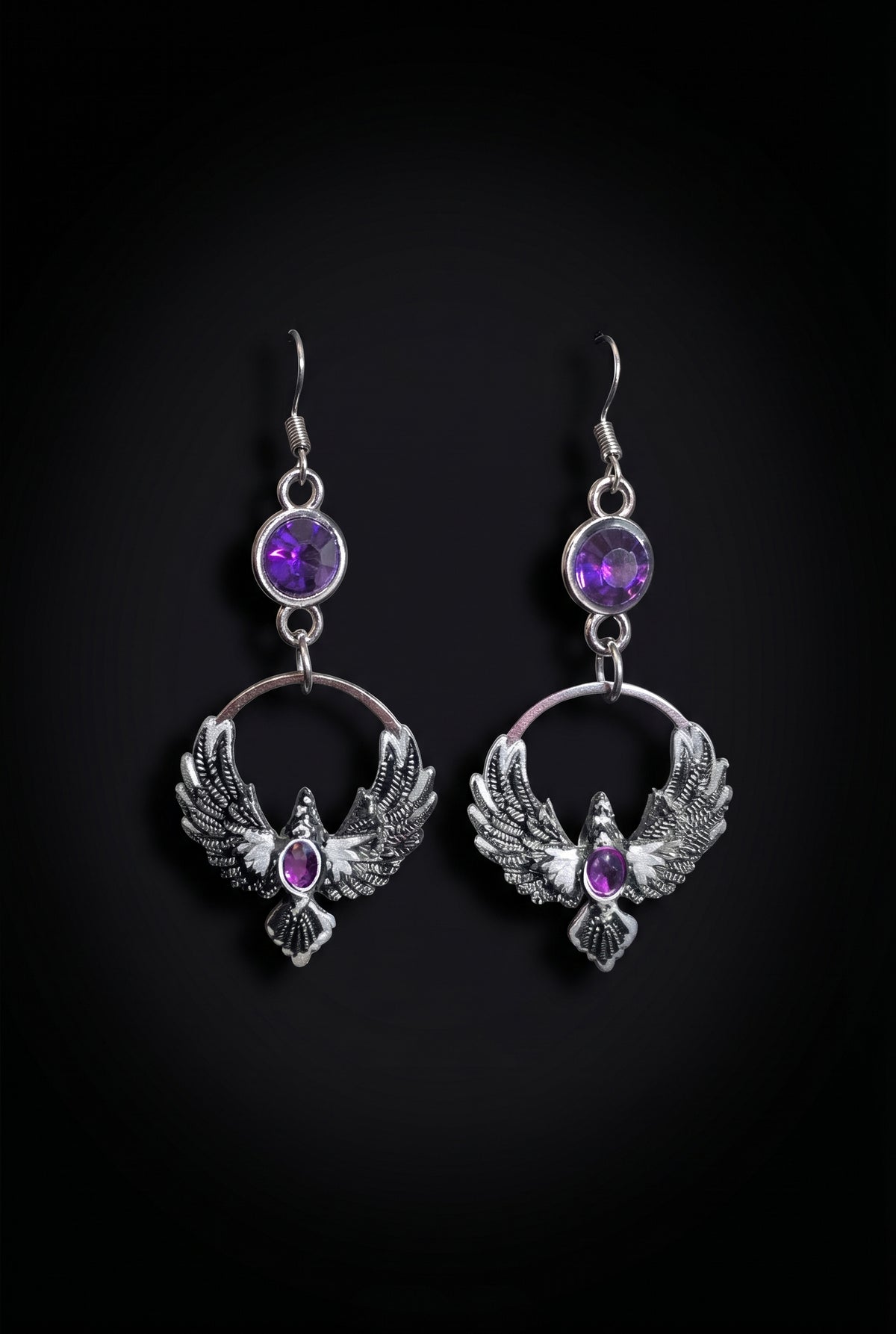 Purple Phoenix Halo Earrings by Circle of Heather, full view of both earrings showing the faceted purple stones, open circles and outstretched feathered wings, on a plain black background.