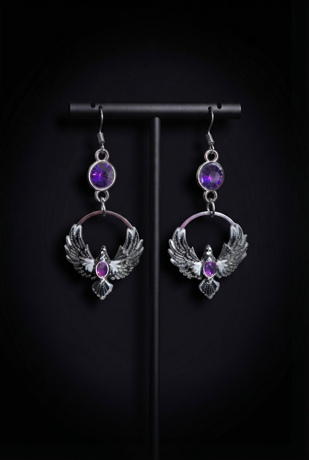 Purple Phoenix Halo Earrings by Circle of Heather, purple stone tops and silver circles with detailed winged bird charms, hanging on a black T-bar jewelry stand against a black background.