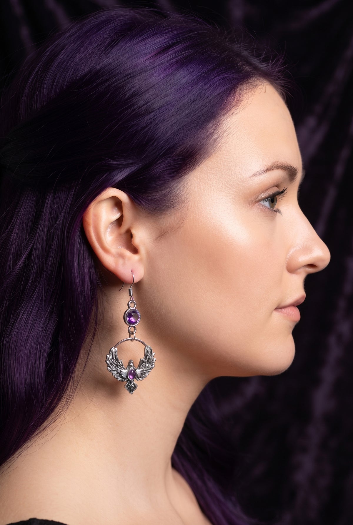 Purple Phoenix Halo Earrings by Circle of Heather worn by a model with long deep purple hair, faceted purple stone above a silver circle holding a winged bird with a purple stone at its chest.