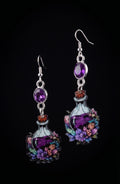 A pair of dangling earrings shaped like small illustrated potion bottles with purple liquid, silver hooks, oval purple stones, and colorful floral details, shown on a black background.