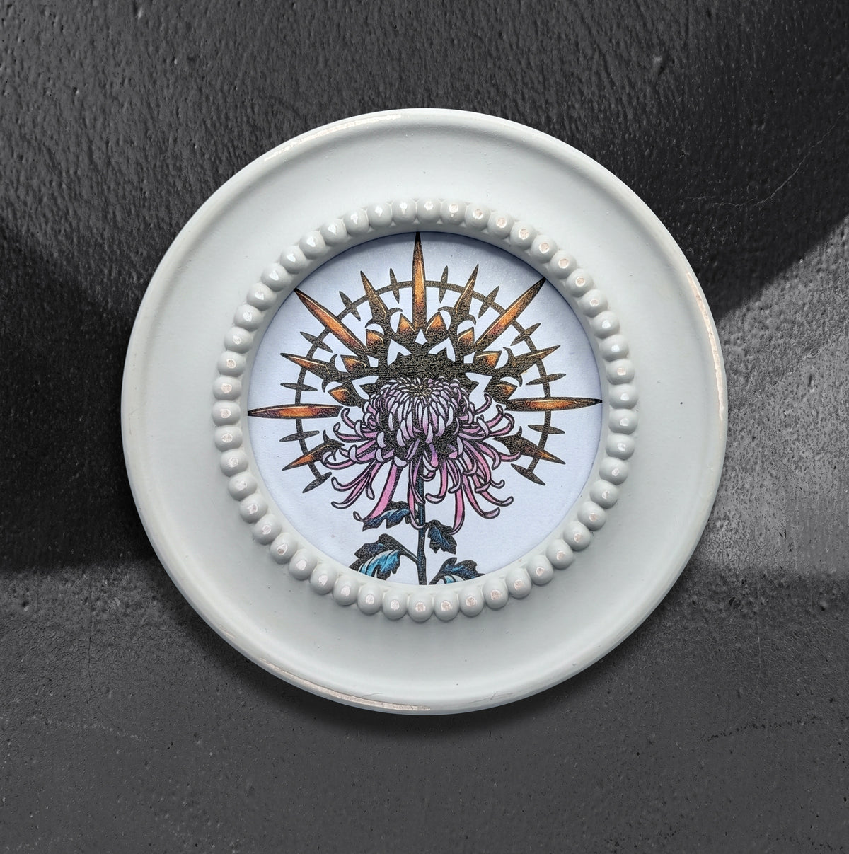 Radial Mum framed print by CamiThunderInk, a round botanical mandala of a chrysanthemum printed on shimmering pearlescent paper, in a cream round frame