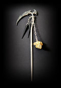Isolated product shot of the silver spine-scythe hair pick against a black background, featuring two short chains with glossy black spikes and a longer chain dangling a weathered bone-colored ram skull charm.
