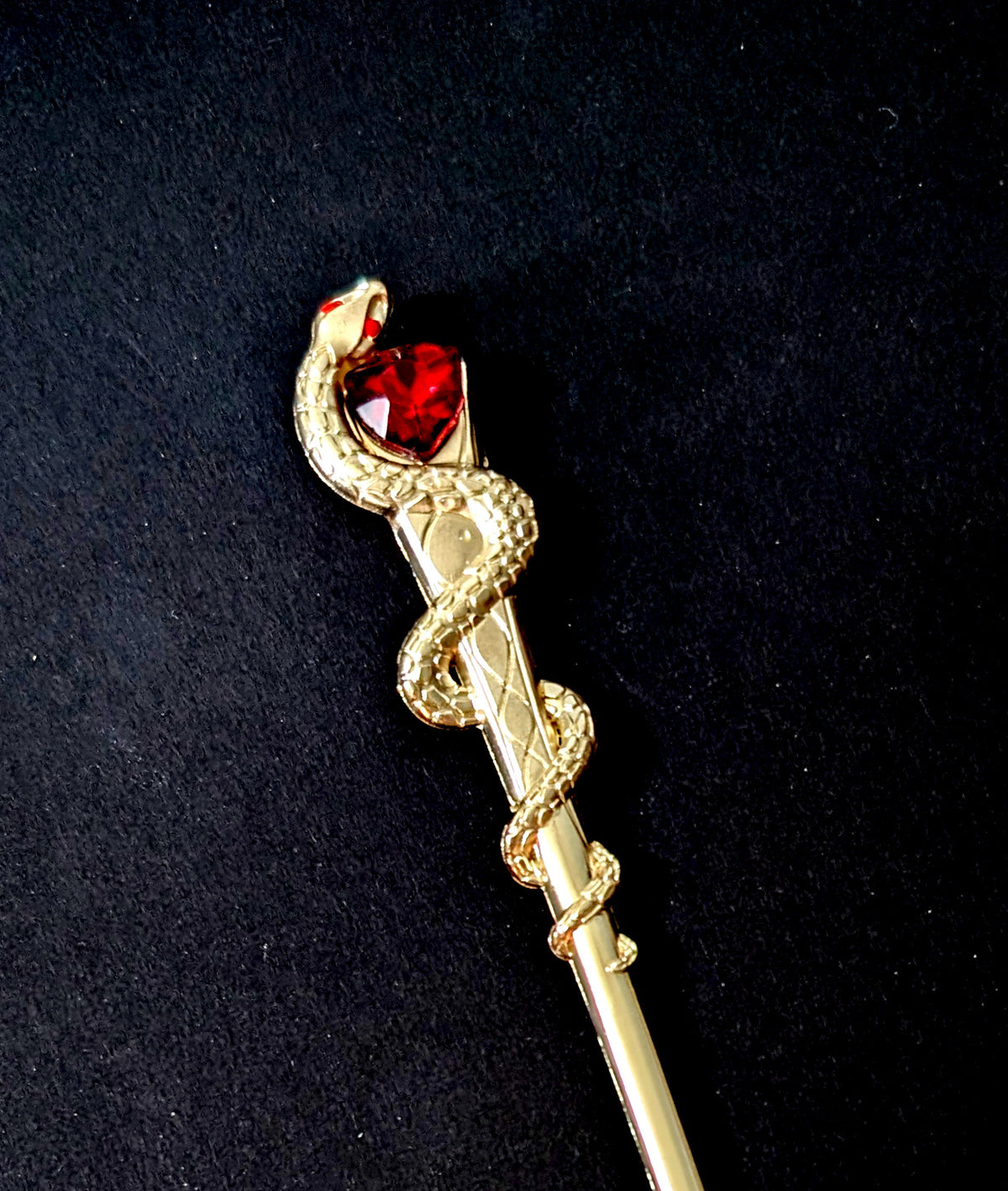 Close-up product shot against a black background, highlighting the detailed scale texture along the coiled gold snake's body and the rich, faceted red heart stone cradled at the top.