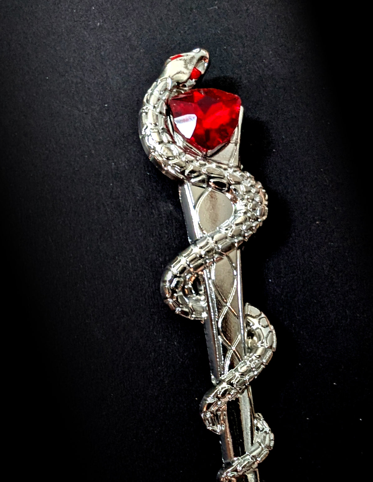 Close-up view of the silver hair pick against a black background, highlighting the detailed scale texture along the coiled snake's body and the bright, faceted red heart stone cradled at the top.