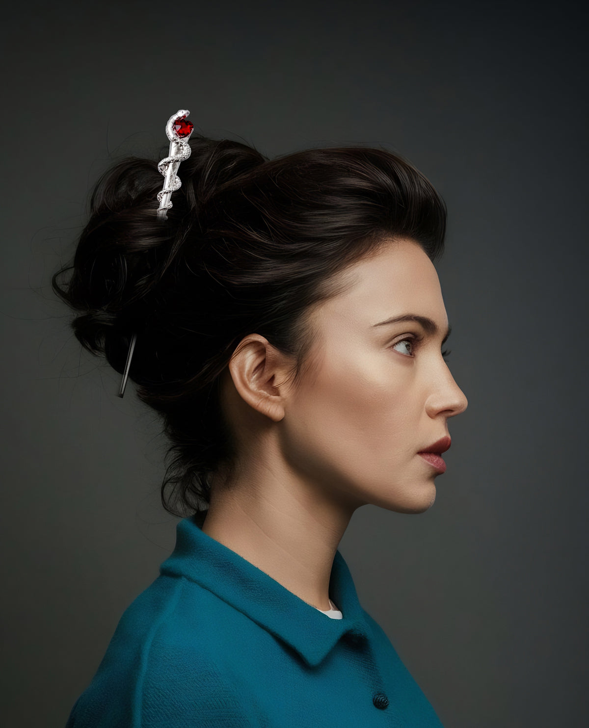 Side profile of a model with dark hair styled in an updo secured by the silver snake and red heart hair pick, wearing a teal collared top against a dark grey background.