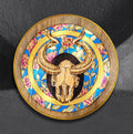 Shimmering Goat Skull by CamiThunderInk, an original pyrography and metallic watercolor painting on a 12 inch pine round of a horned goat skull inside a ring of peonies, with a gold border and stippled black halo
