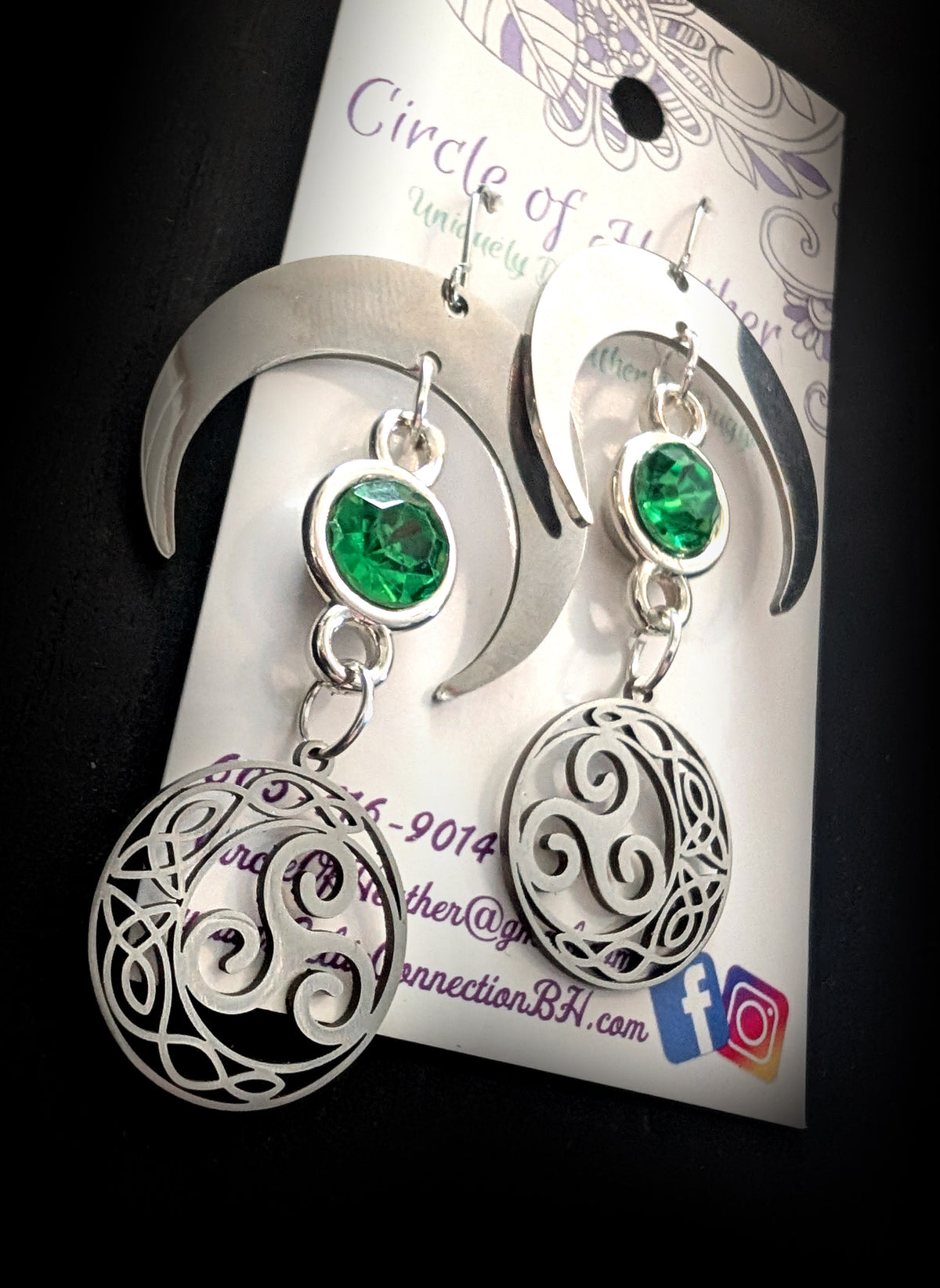 Shimmer Lunar Nocturne Earrings by Circle of Heather, angled close-up of the green faceted stones inside the silver crescents with openwork triple spiral medallions below, shown on the branded Circle of Heather card.