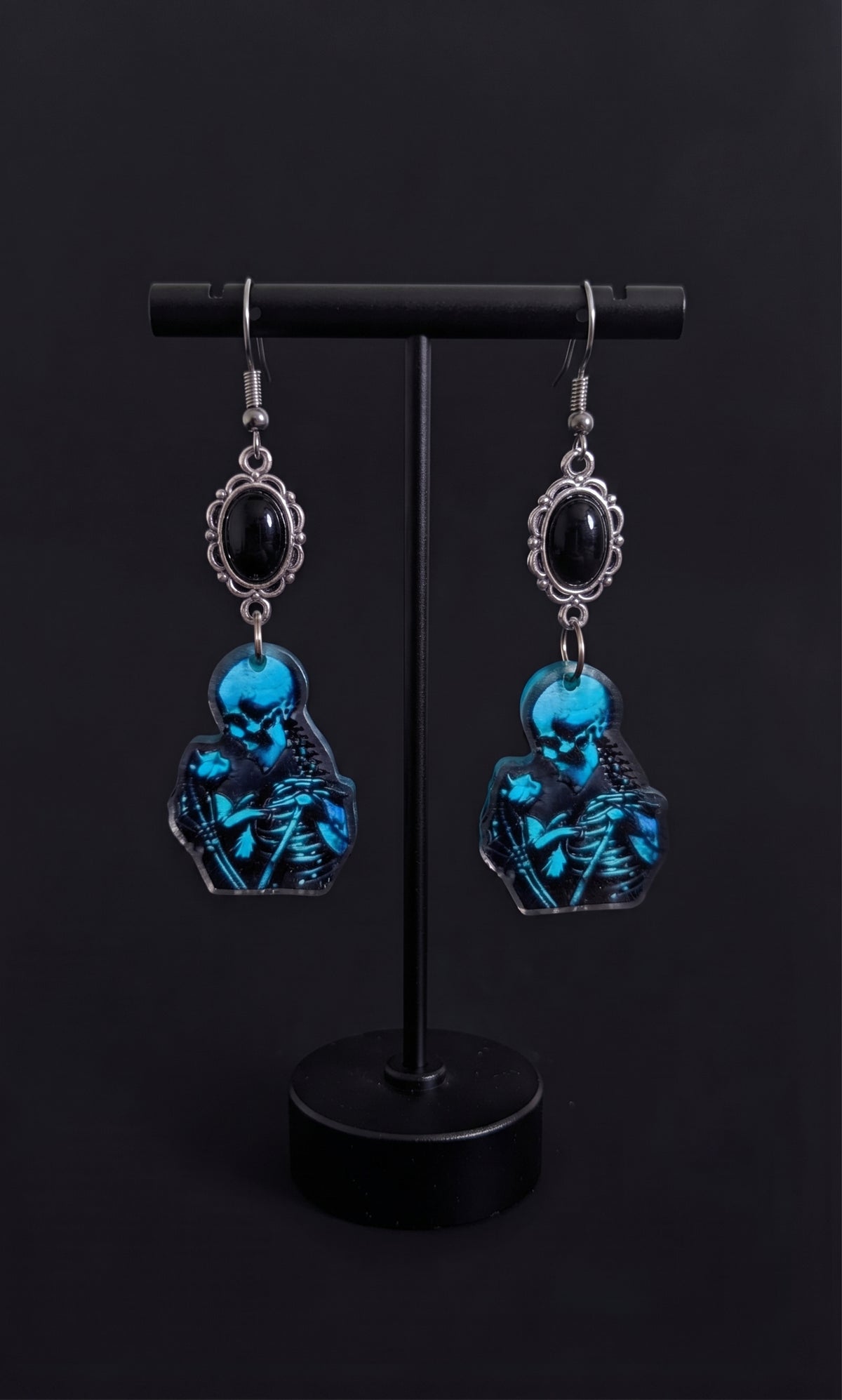 Skele Kitty Snuggles Earrings by Circle of Heather, close-up of the blue and black artwork showing the skull, spine and ribcage detail, shown on the branded Circle of Heather card.